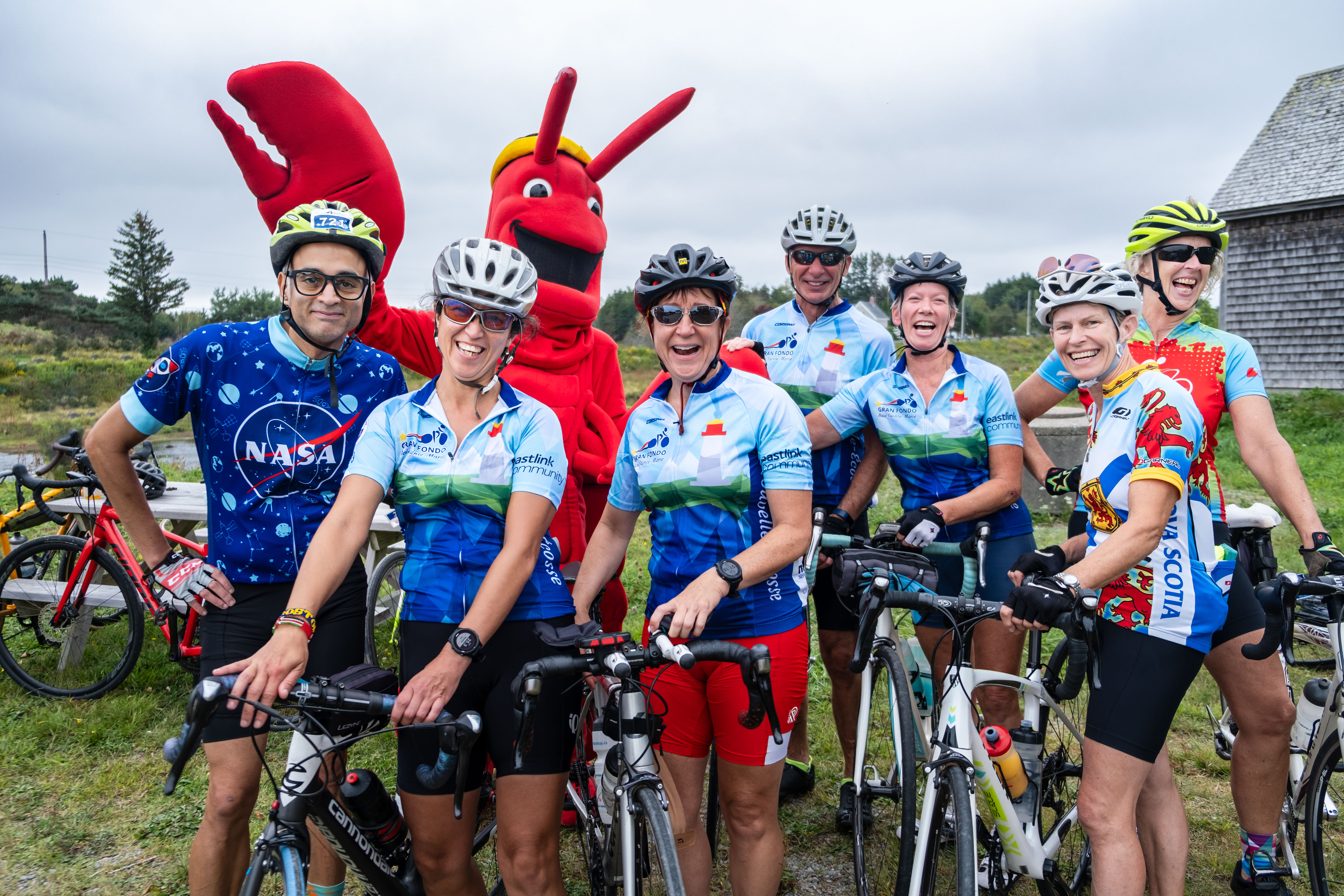Un groupe de cyclistes avec la mascotte homard en arrière-plan, au point de repos du moulin à Bangor pendant le Gran Fondo 2023.