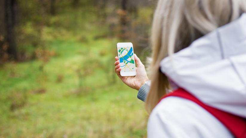 photo d'une femme qui tiend un GPS et marche dans la forêt